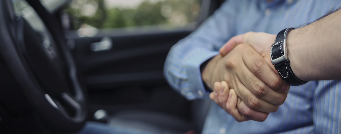 Two person are shown shaking hands in a vehicle.