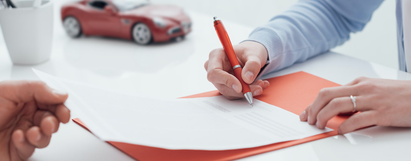 A person is shown signing paper in front of a toy car.