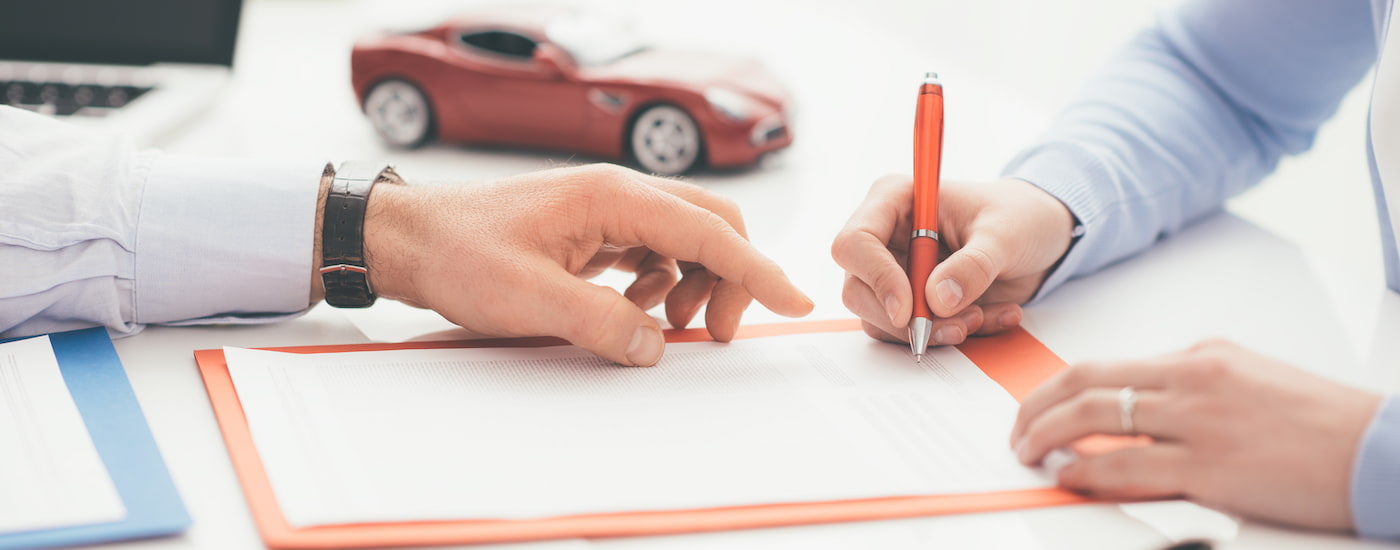 A person is shown signing paper in front of a toy car.