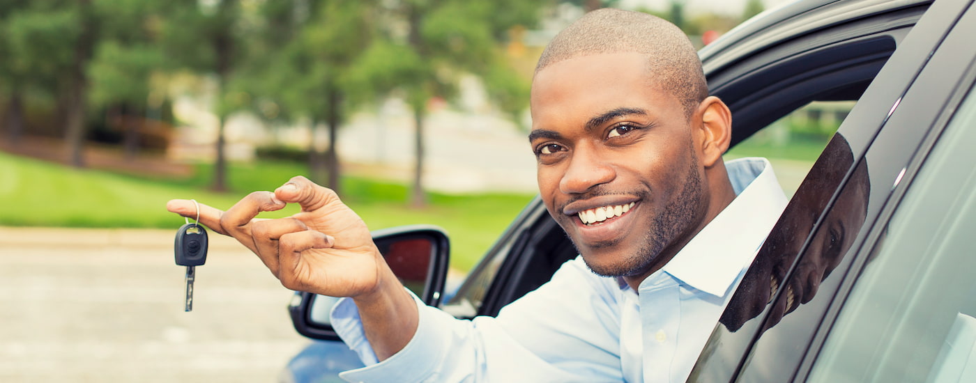 A person is shown holding out a car key through their car window.