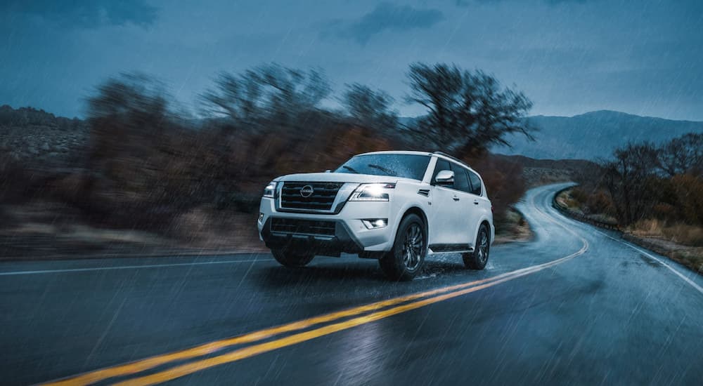 A white 2022 Nissan Armada is shown driving on a winding road during a rainstorm.