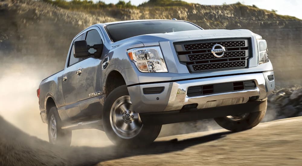 A silver 2021 Nissan Titan XD is shown driving on a dusty dirt road.
