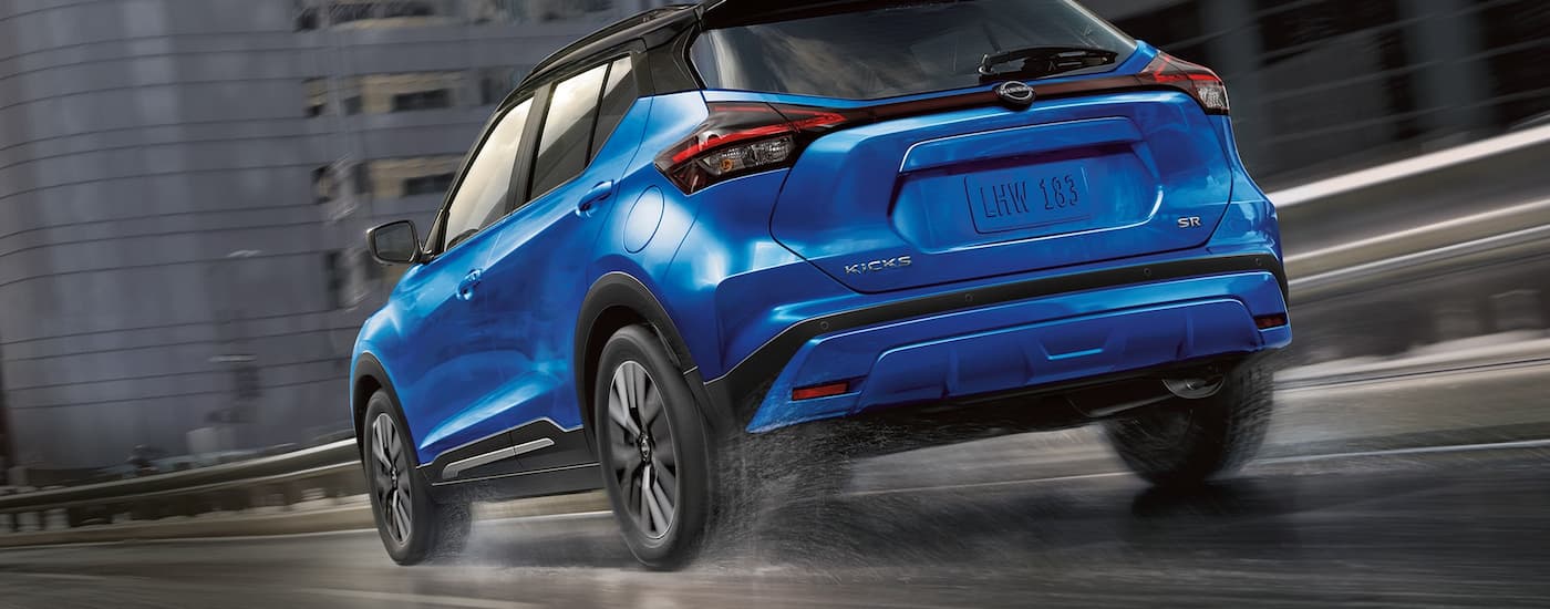 A blue 2022 Nissan Kicks is shown from the rear driving on a city highway after a rain storm.