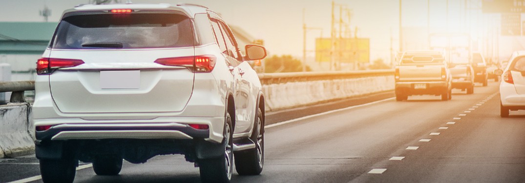 Rear passenger angle of a white car driving on the highway with a sunrise in the background