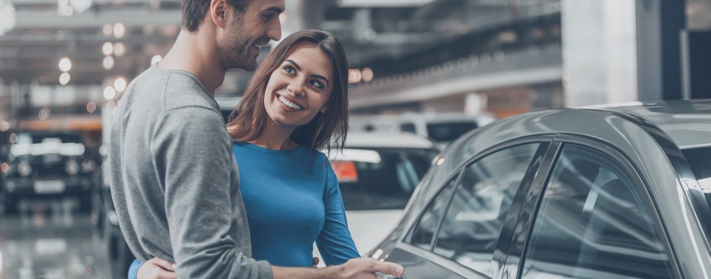 A smiling couple is shown looking at vehicles.