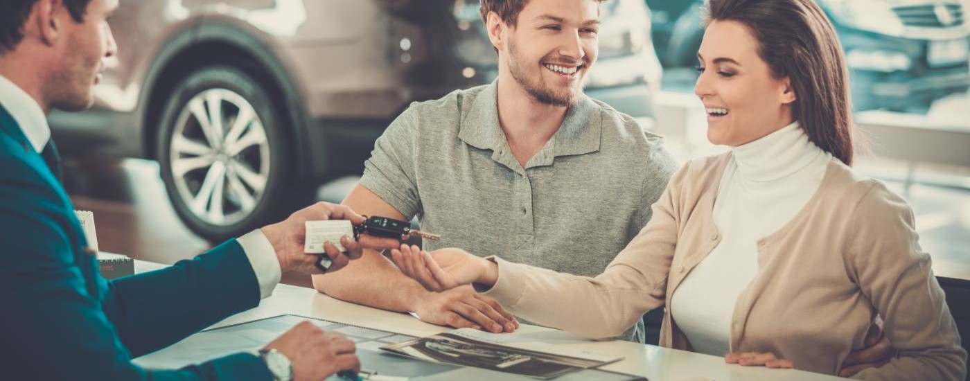 A salesperson is shown handing keys to a smiling couple.