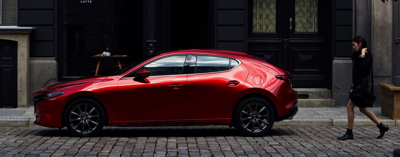 A red 2023 Mazda3 for sale is shown in front of a coffee shop.