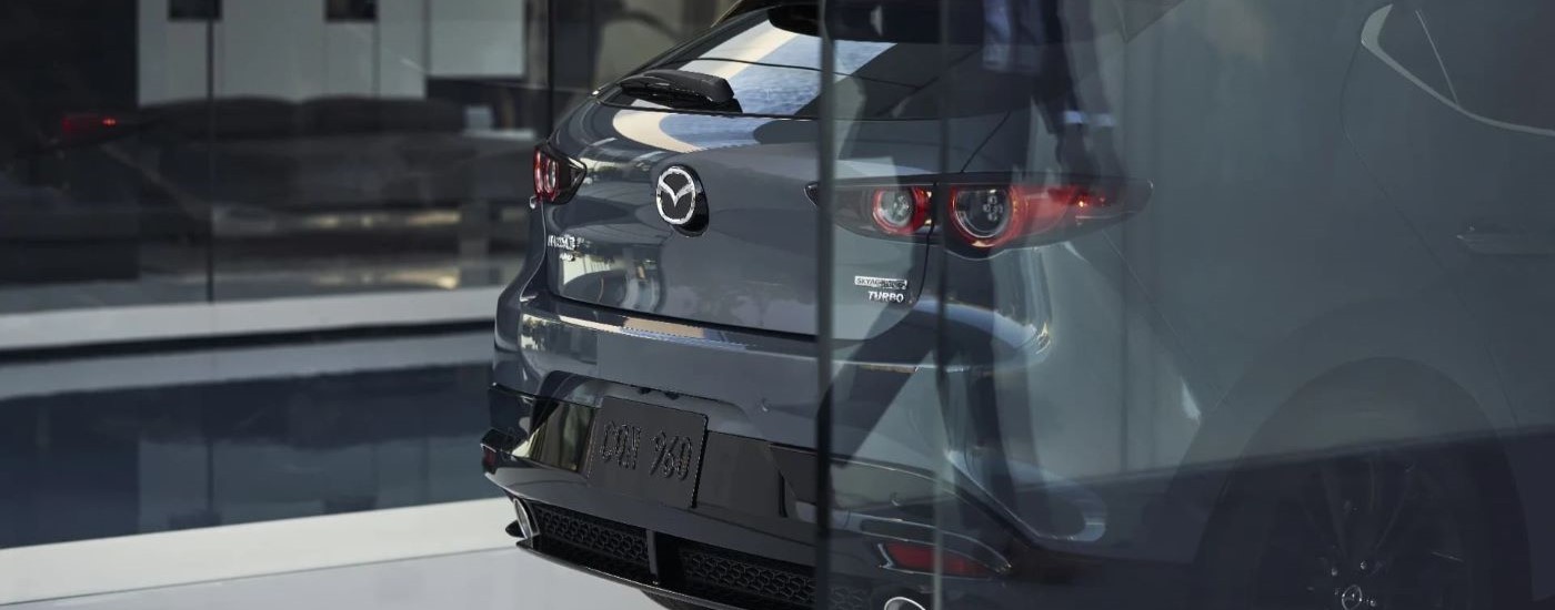 A grey 2022 Mazda3 is shown from the rear behind glass.