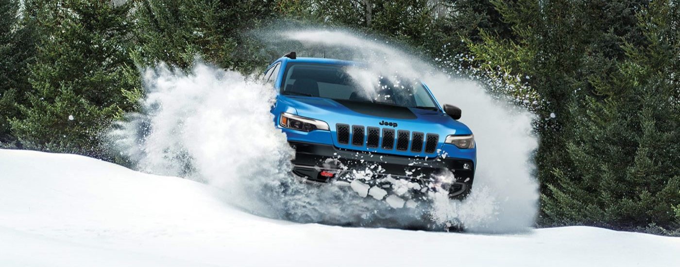 A blue 2023 Jeep Cherokee Trailhawk is shown driving through the snow.