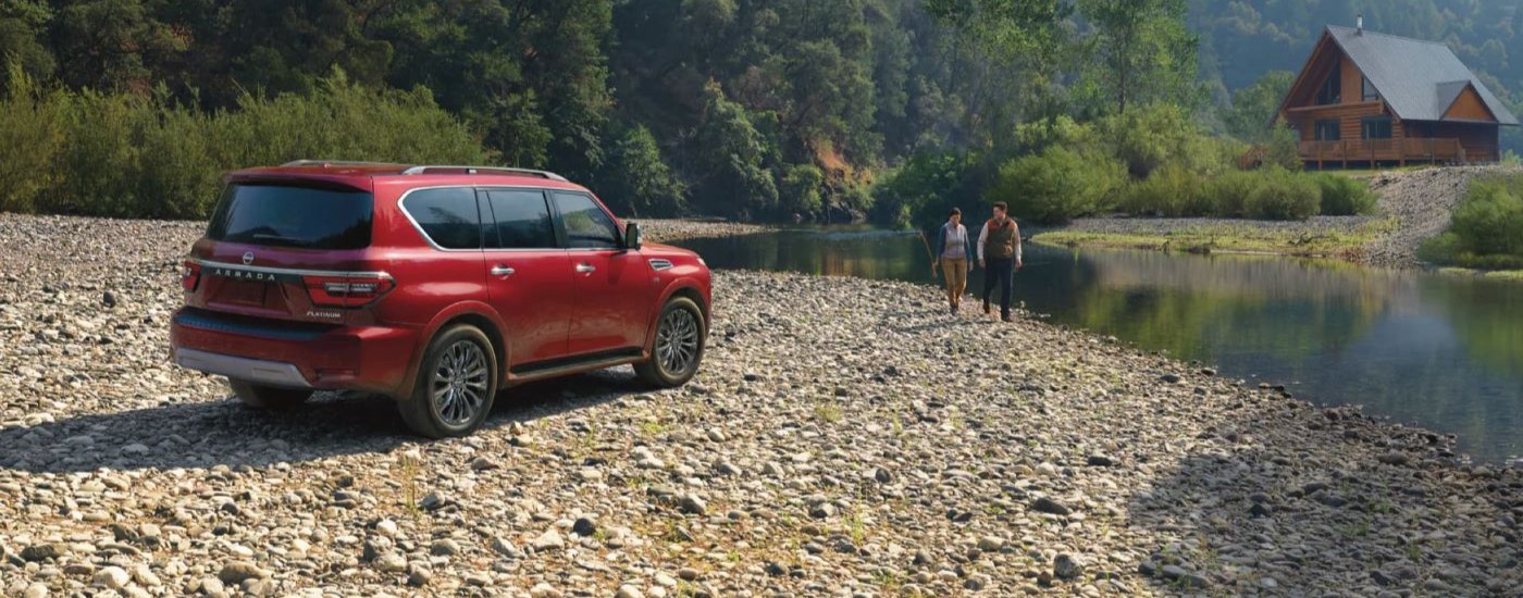 A red 2023 Nissan Armada Platinum is shown parked next to a river and a cabin.