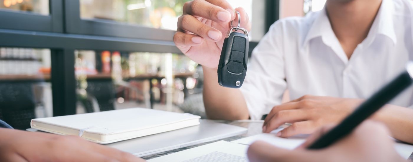 A key fob is shown being passed to a customer at a dealership.
