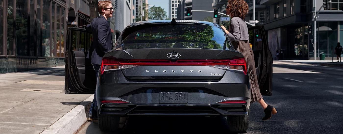 A couple is shown getting into a dark grey 2023 Hyundai Elantra Limited on a city street.