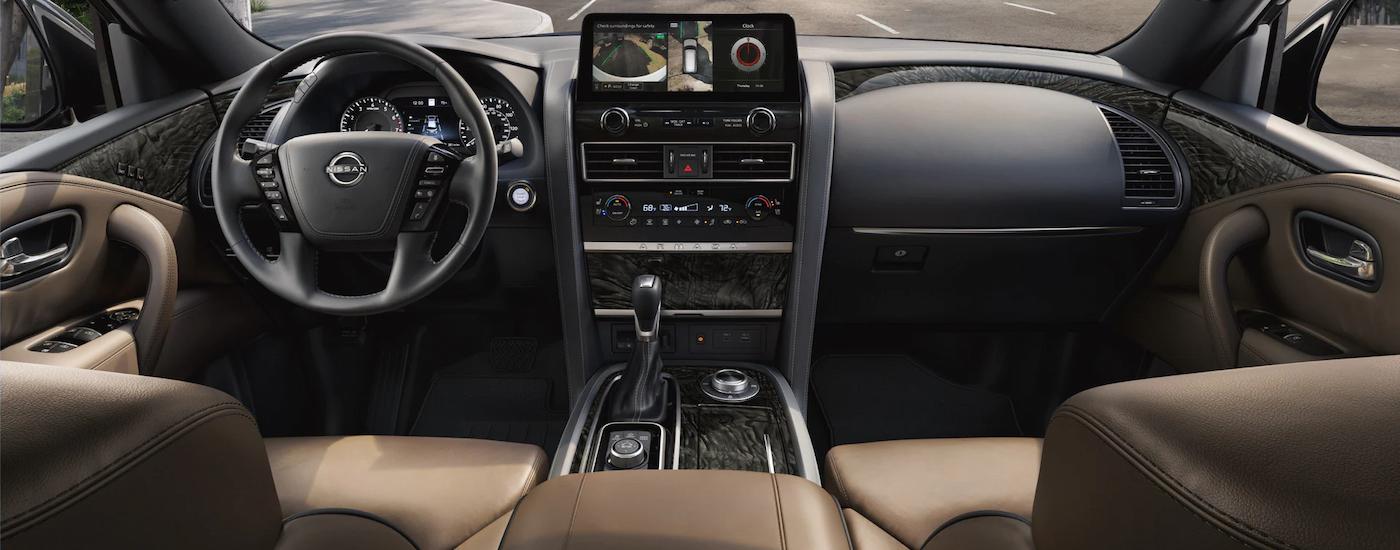 The black and tan interior of a 2023 Nissan Armada Platinum shows the steering wheel and center console.