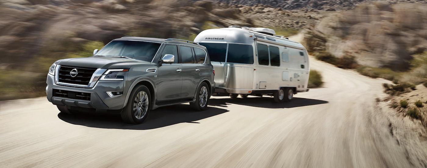 A grey 2023 Nissan Armada Platinum is shown towing a camper trailer on a winding dirt road.