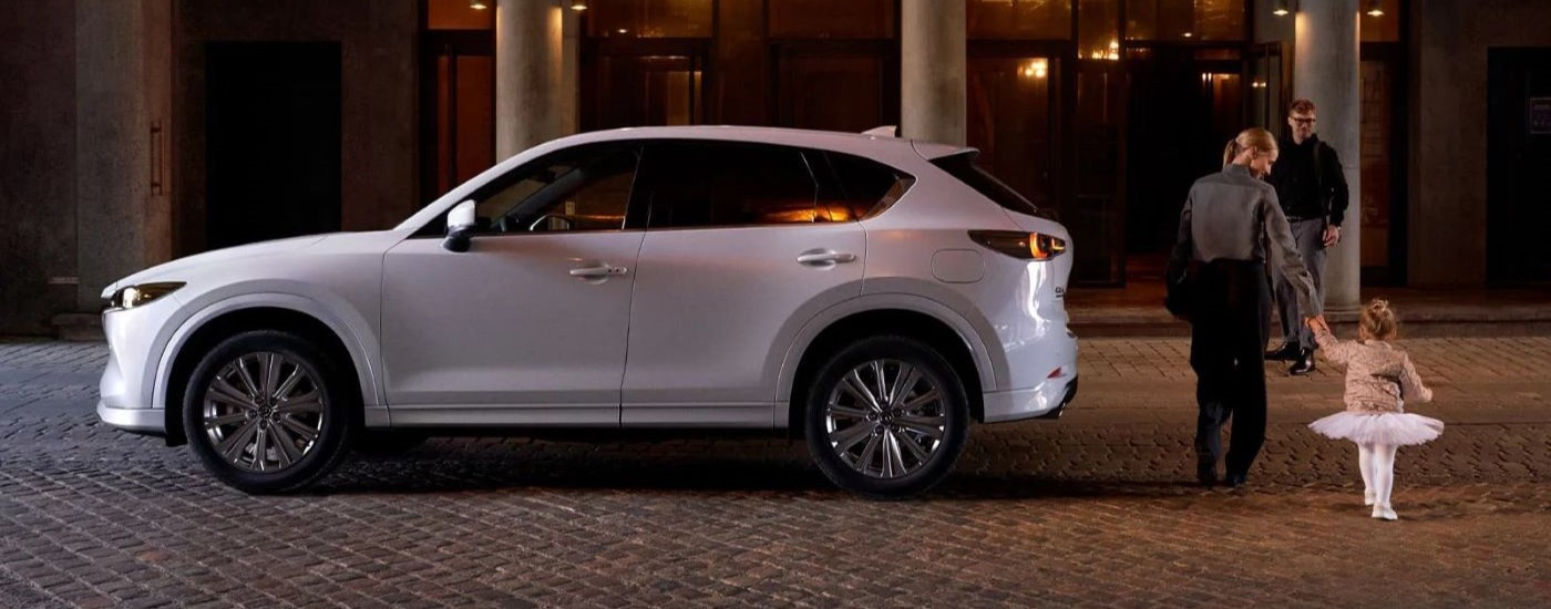 A whtie 2022 Mazda CX-5 is shown next to a family entering a building.