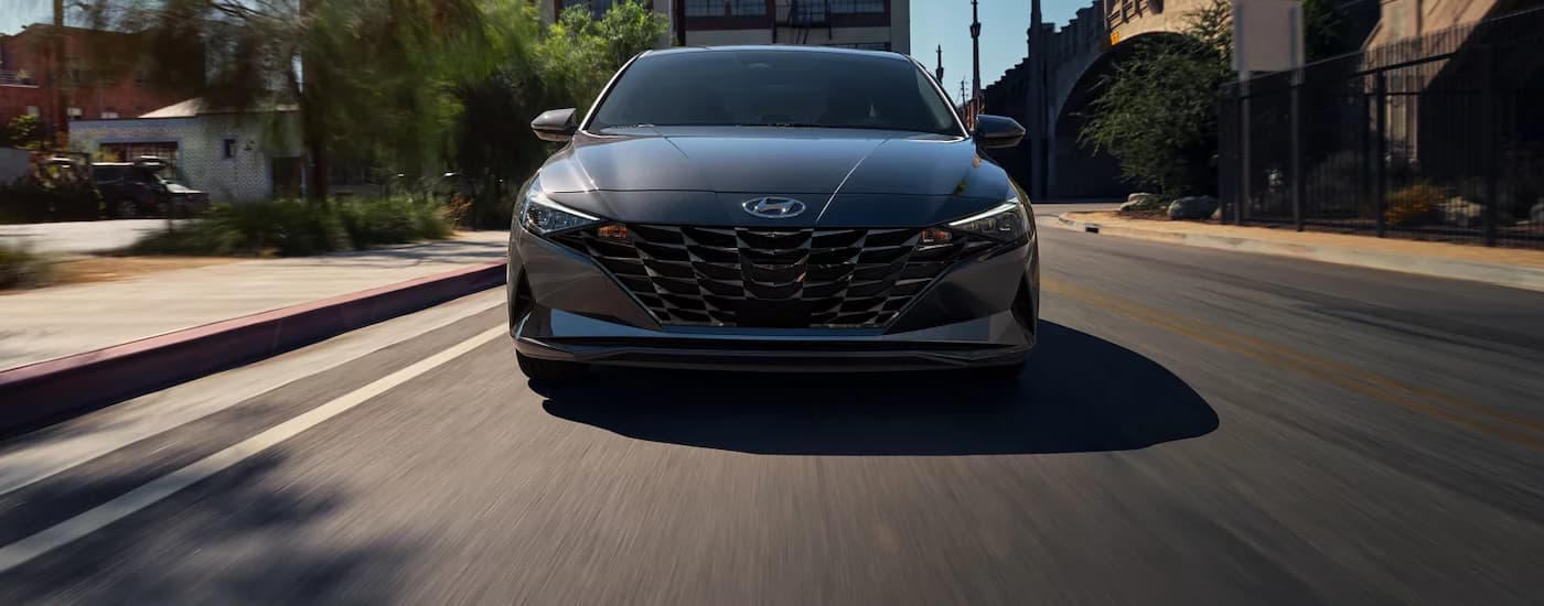 A grey 2023 Hyundai Elantra for sale is shown from the front driving on a city street.