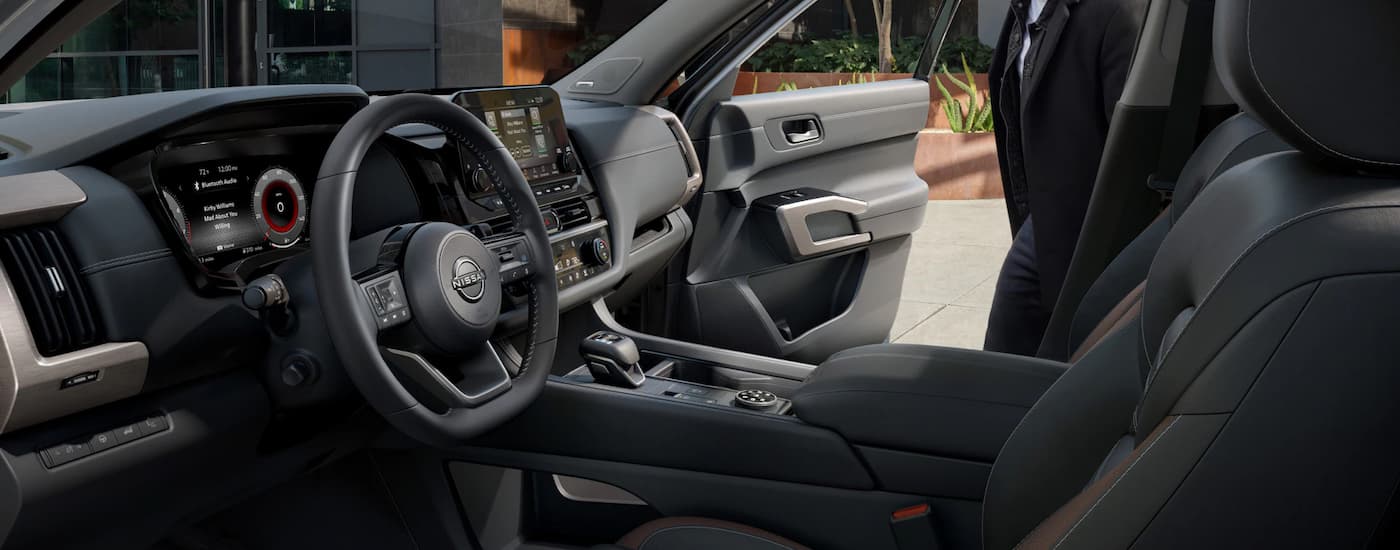 The black interior of a 2023 Nissan Pathfinder shows the steering wheel and center console.