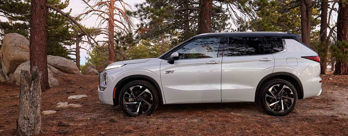 A white 2023 Mitsubishi Outlander PHEV is shown from the side parked in the woods.