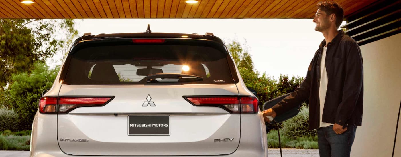 A white 2023 Mitsubishi Outlander PHEV is shown charging in a garage.