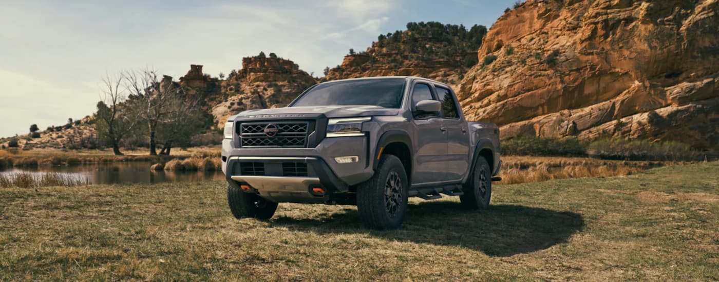 A grey 2023 Nissan Frontier for sale, is shown parked in a field.