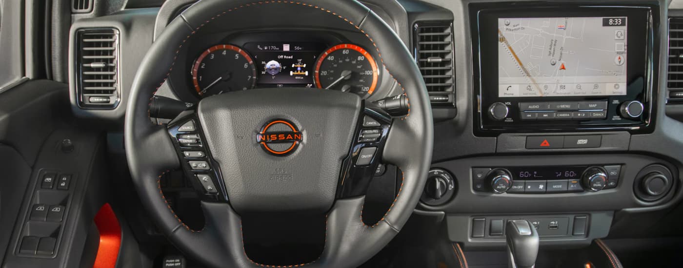 The grey interior of a 2023 Nissan Frontier shows the steering wheel and infotainment screen.