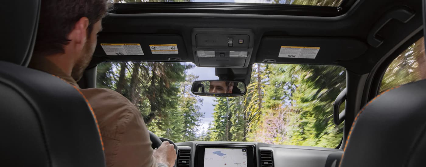 A person is shown driving a 2023 Nissan Frontier on a forest road.