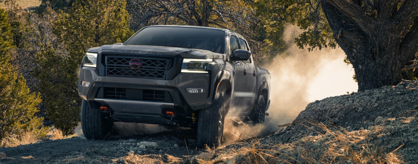 A grey 2023 Nissan Frontier for sale, is shown off-roading on a dirt path. 
