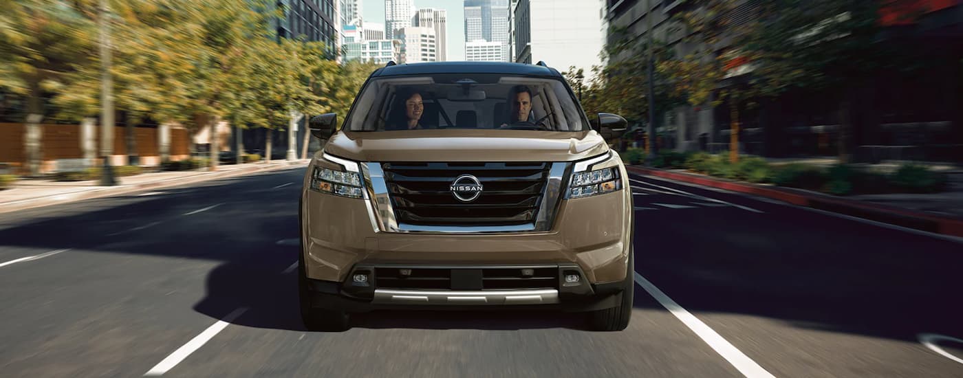 A tan 2023 Nissan Pathfinder is shown driving through a city.