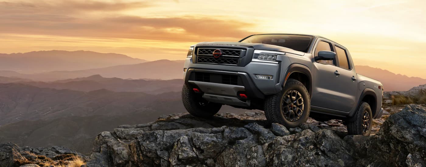 A grey 2023 Nissan Frontier is shown from the side parked on a mountain at sunset.