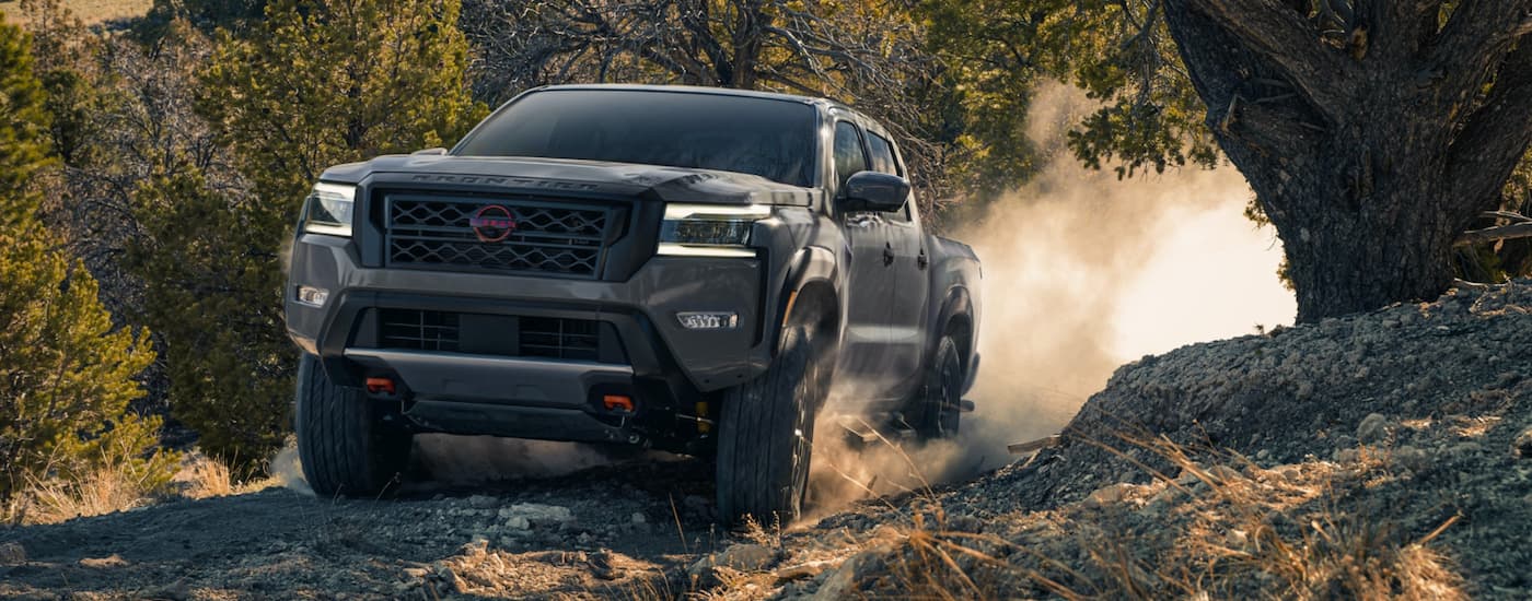 A grey 2023 Nissan Frontier is shown from the front driving on a dirt road.