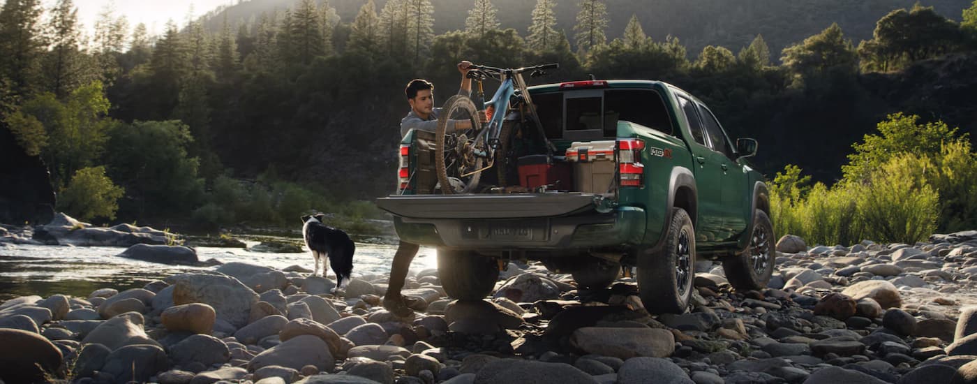 A popular Nissan Frontier for sale, a green 2023 Nissan Frontier is shown from the rear parked on a river bank.