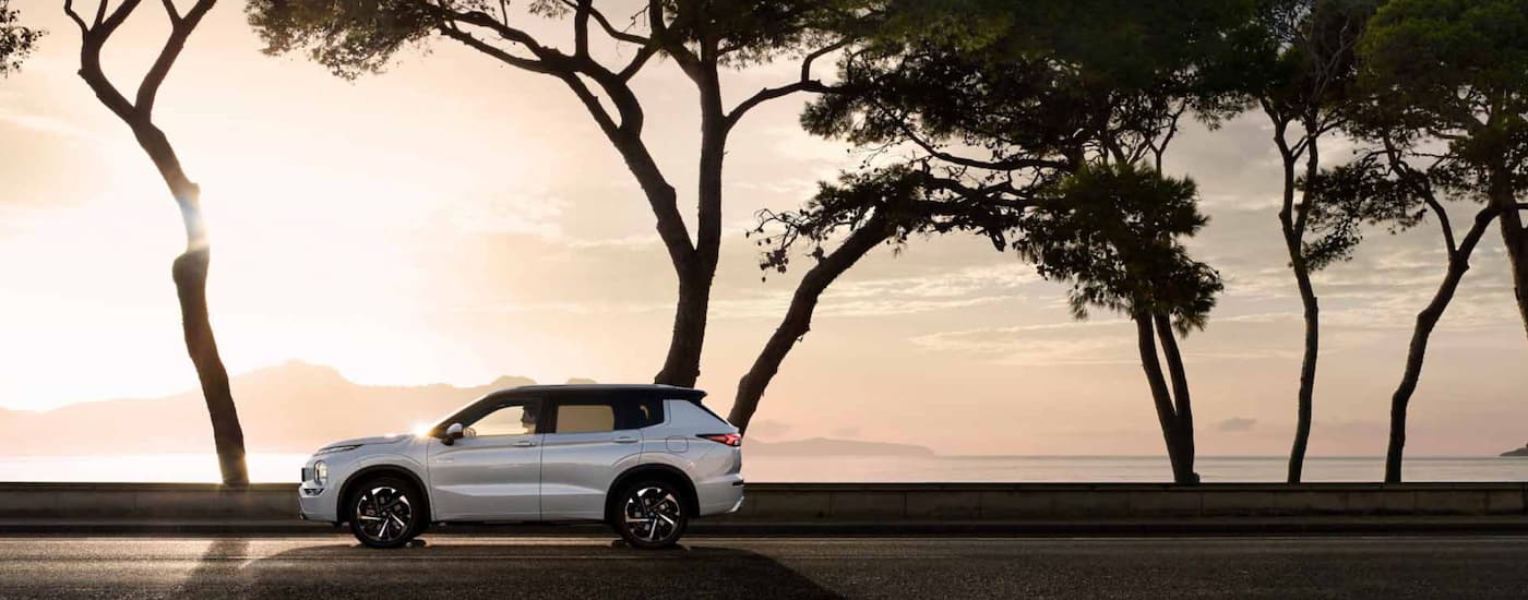 A white 2023 Mitsubishi Outlander PHEV is shown from the side driving at sunset.