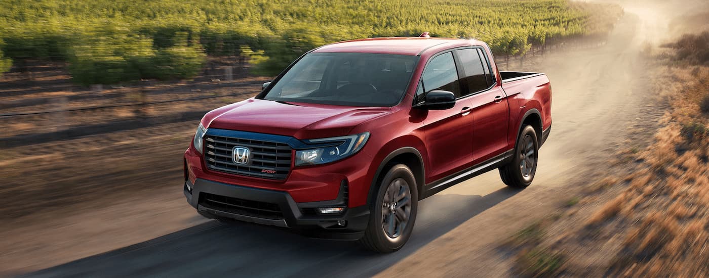 A red 2022 Honda Ridgeline is shown driving on a dusty dirt road after leaving a Honda dealer.
