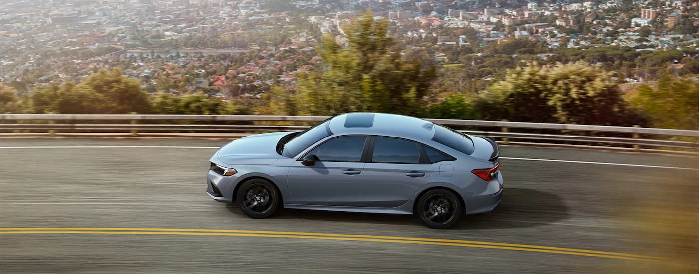 A grey 2022 Honda Civic Si is shown from the side driving on a mountain highway after leaving a Honda dealer.