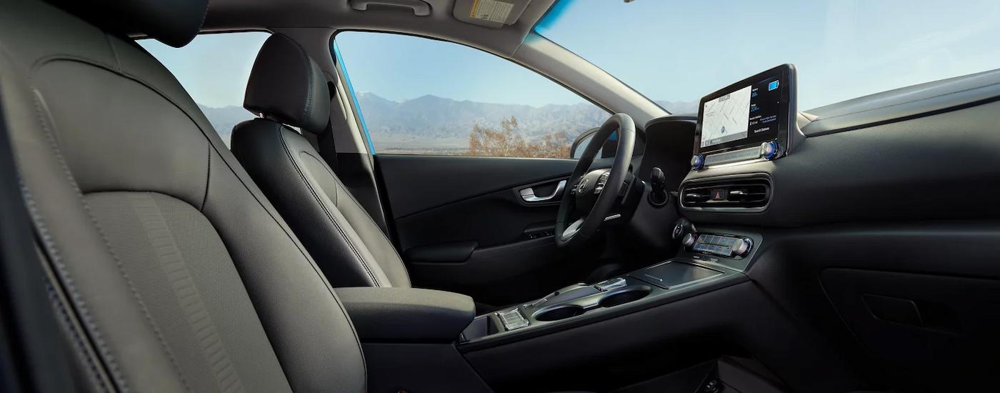 The grey interior of 2023 Hyundai Kona EV shows the center console and front seating.
