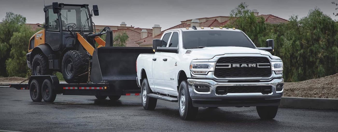 A white 2020 Ram 2500 is shown from the front towing heavy machinery.