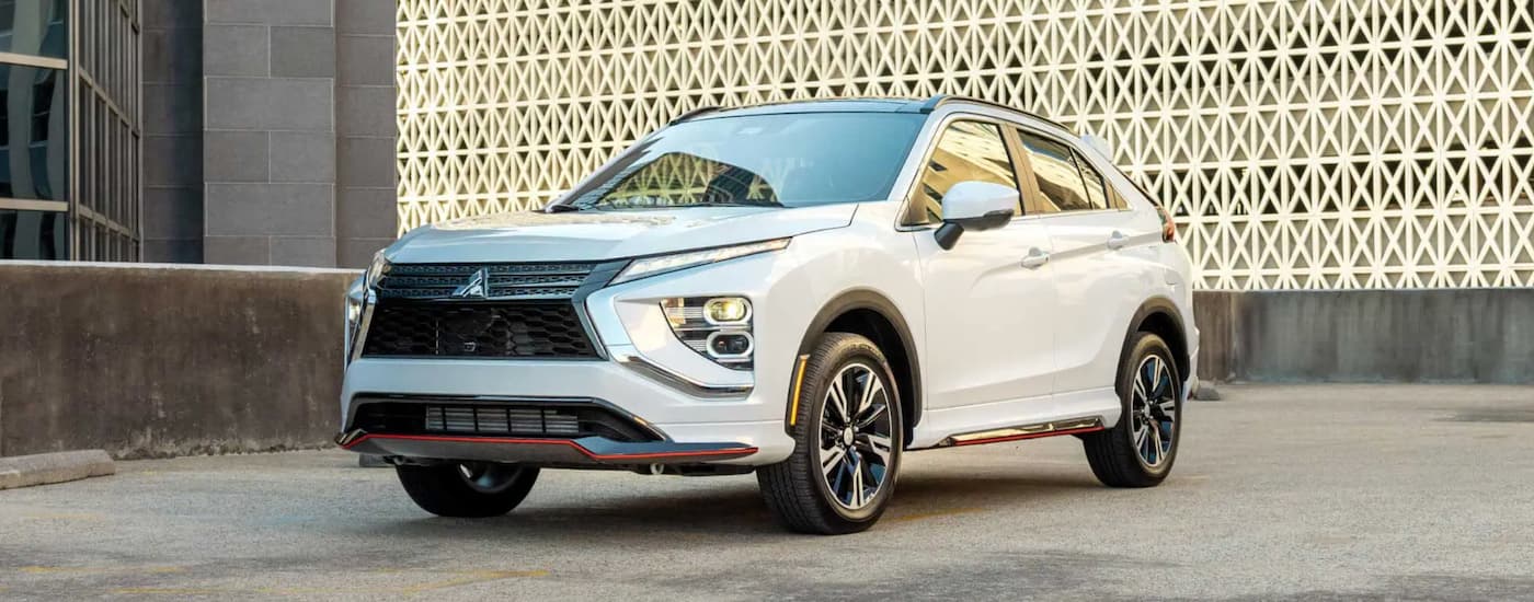 A white 2023 Mitsubishi Eclipse Cross is shown from the front parked in front of a modern building.
