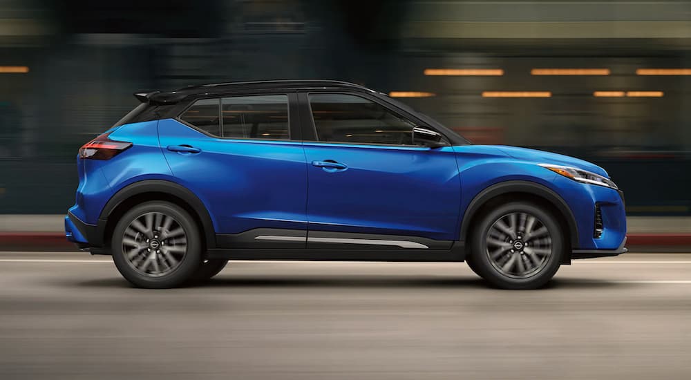 A blue 2023 Nissan Kicks is shown from the side driving on an open road.