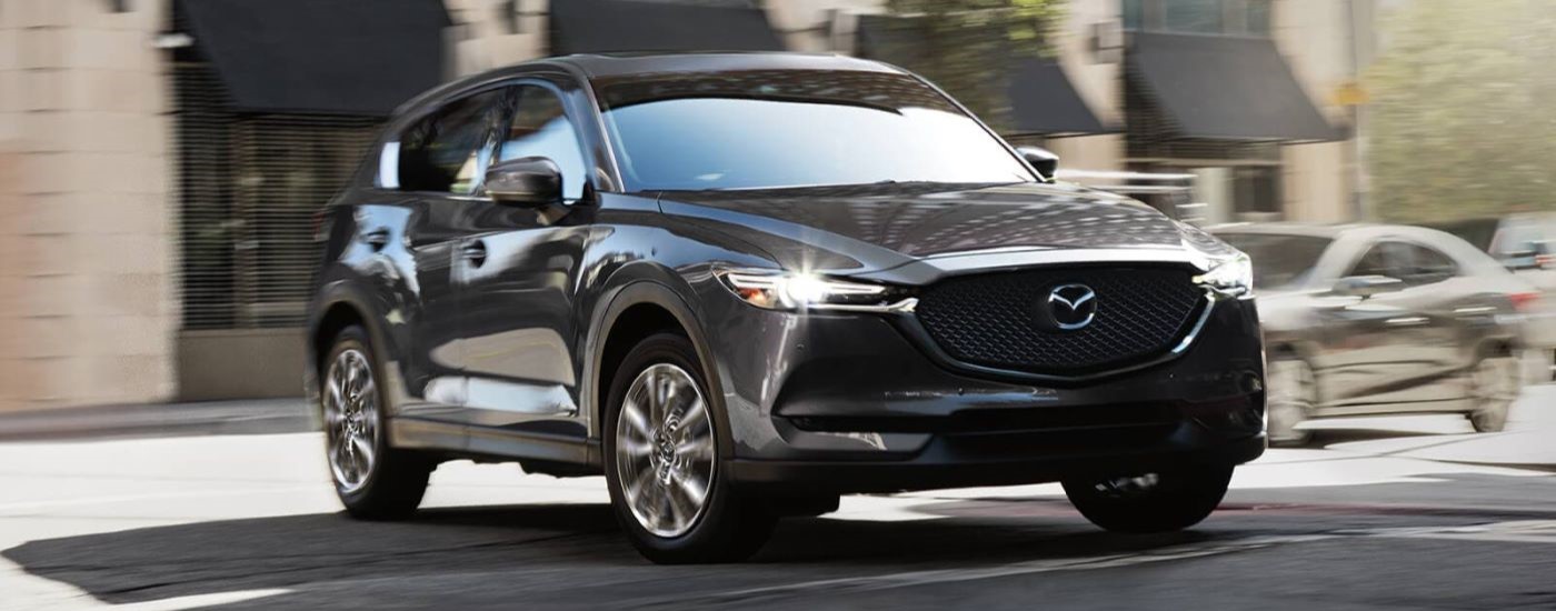 A dark grey 2021 Mazda CX-5 is shown driving on a city street.