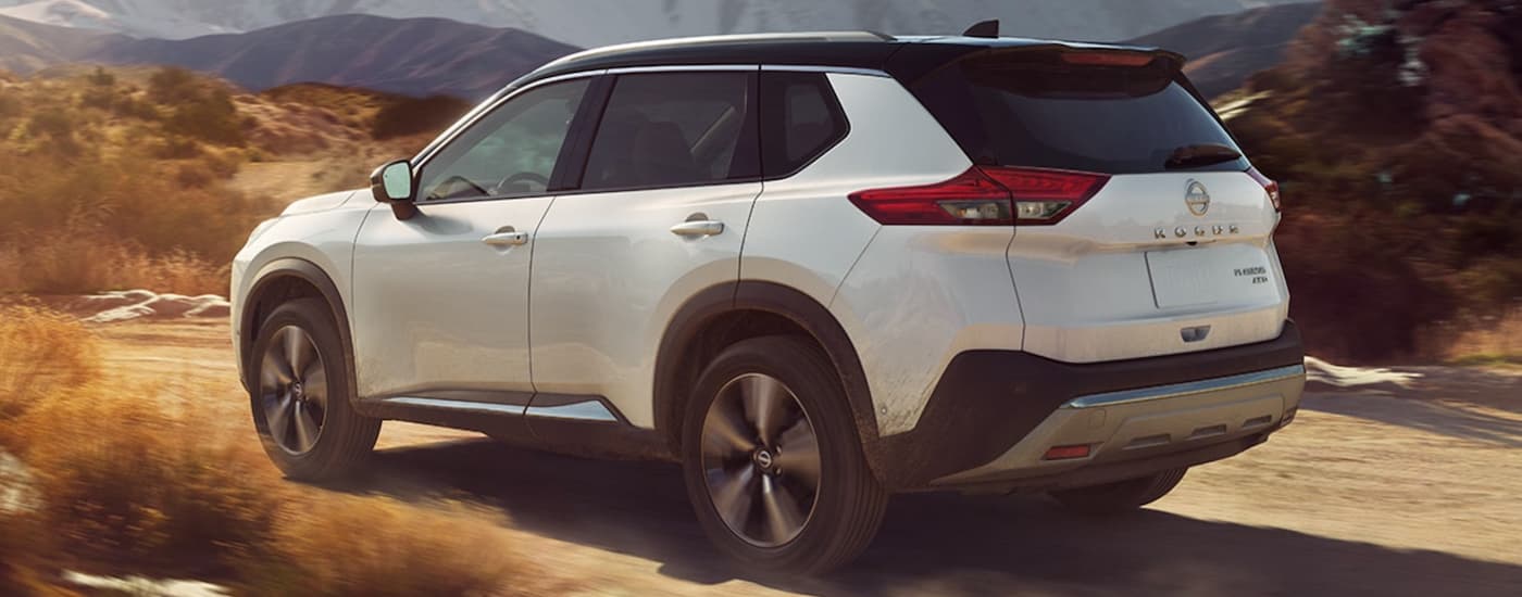 A white 2023 Nissan Rogue is shown from the side driving on a dirt road.