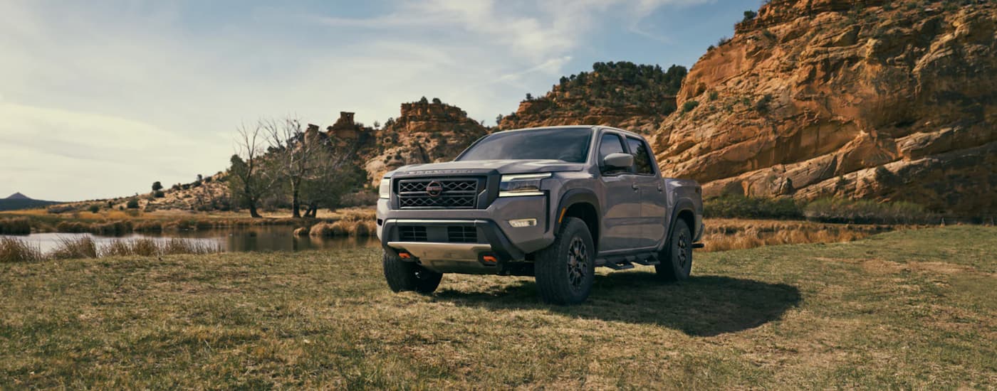 A popular Nissan frontier for sale, a grey 2023 Nissan Frontier, is shown from the front parked in a grass field.
