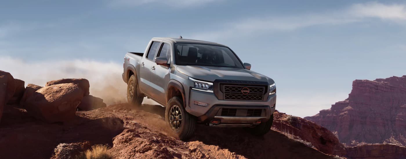 A grey 2023 Nissan Frontier is shown off-roading in the mountains.