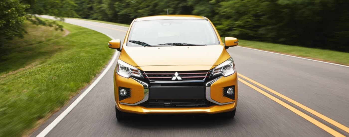 A yellow 2023 Mitsubishi Mirage is shown driving from the front on an open road.