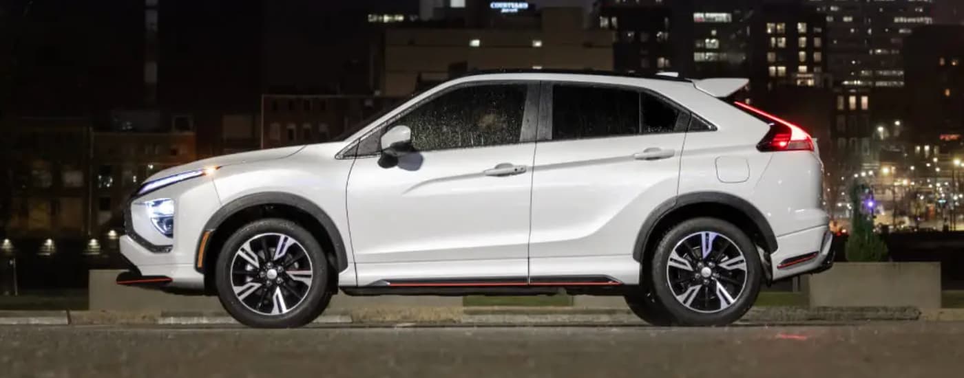 A white 2023 Mitsubishi Eclipse Cross is shown from the side parked in a city at night.