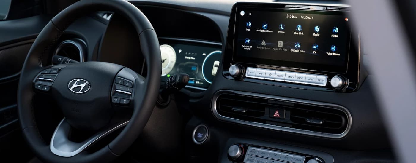 The black interior of a 2023 Hyundai Kona Electric shows the steering wheel and infotainment screen.