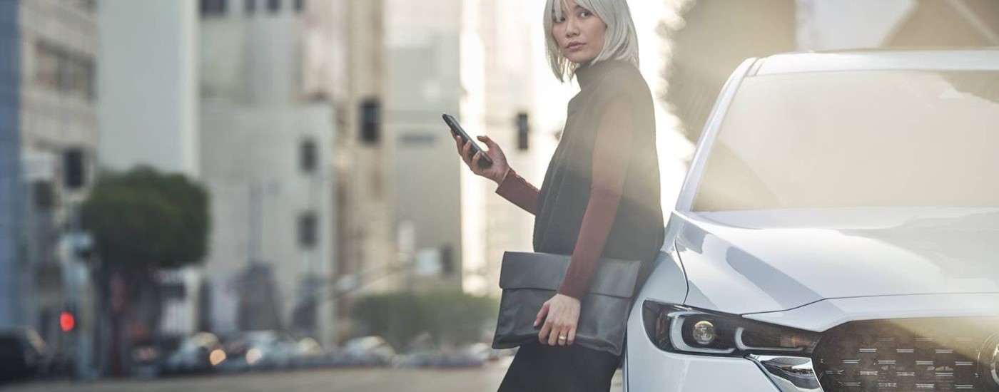 A person holding a phone is shown leaning against a white 2023 Mazda CX-5.