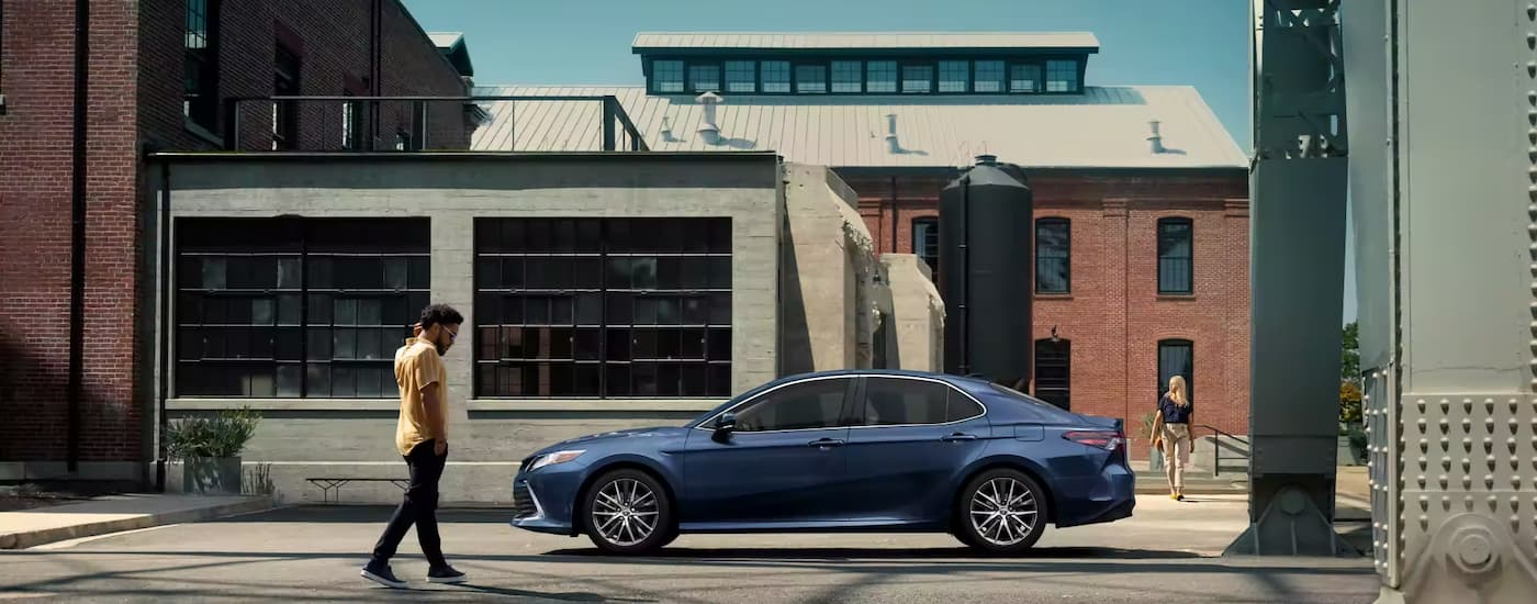 A blue 2023 Toyota Camry parked in front of an urban industrial building
