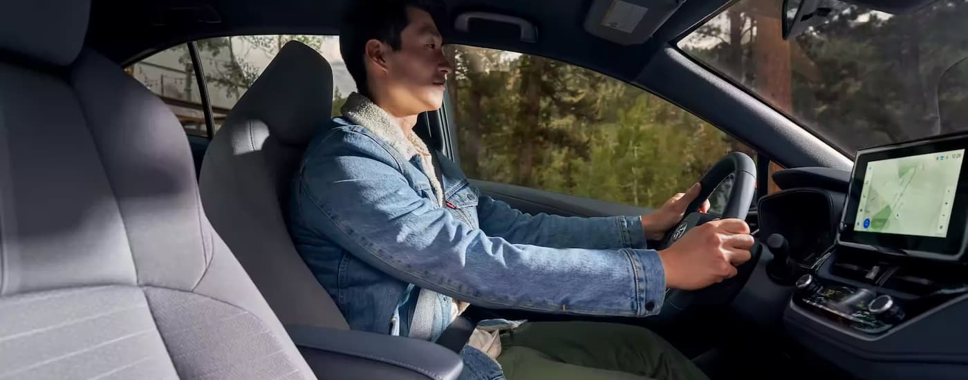 A man is shown from the side driving in a 2023 Toyota Corolla SE Hybrid on a tree-lined road.