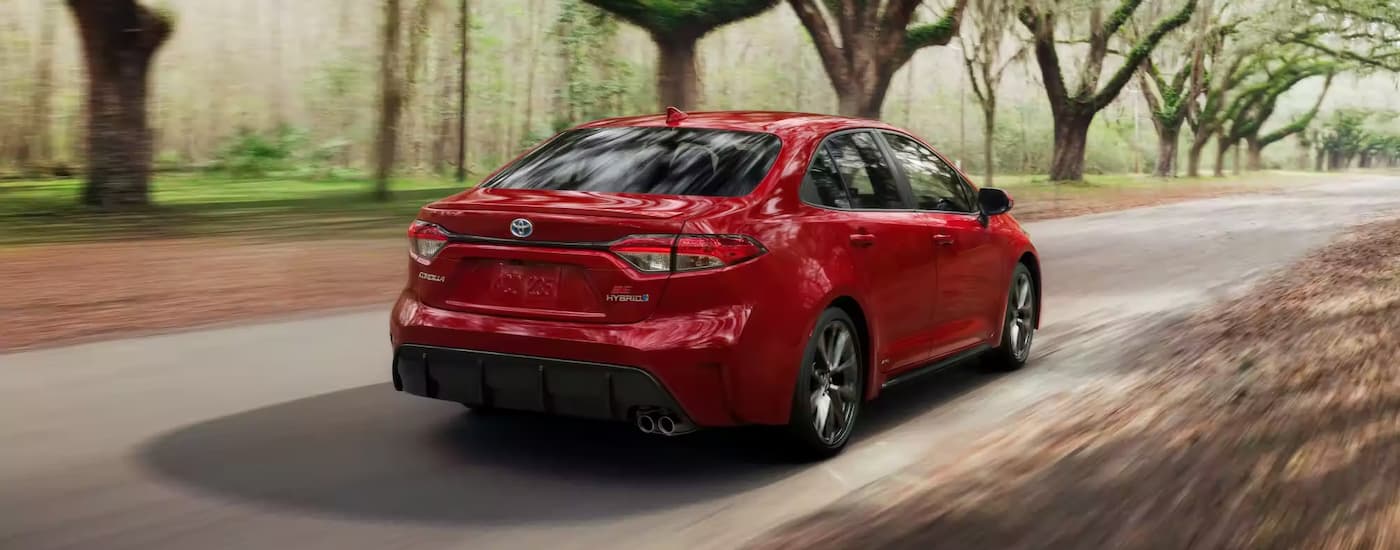 A red 2023 Toyota Corolla SE Hybrid is shown from the rear driving on an open road.