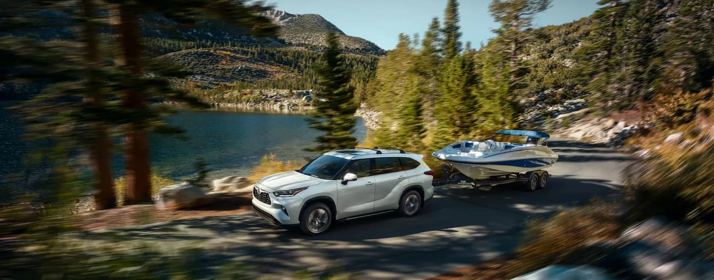 A white 2022 Toyota Highlander towing a boat past an alpine lake.